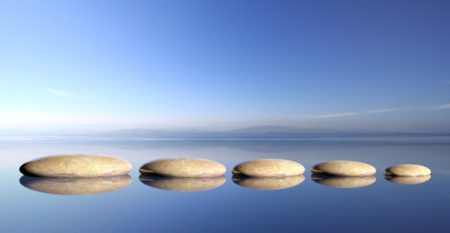 Zen stones row from large to small in water with blue sky and peaceful landscape background. Zen stones row from large to small in water with blue sky and peaceful landscape background.
